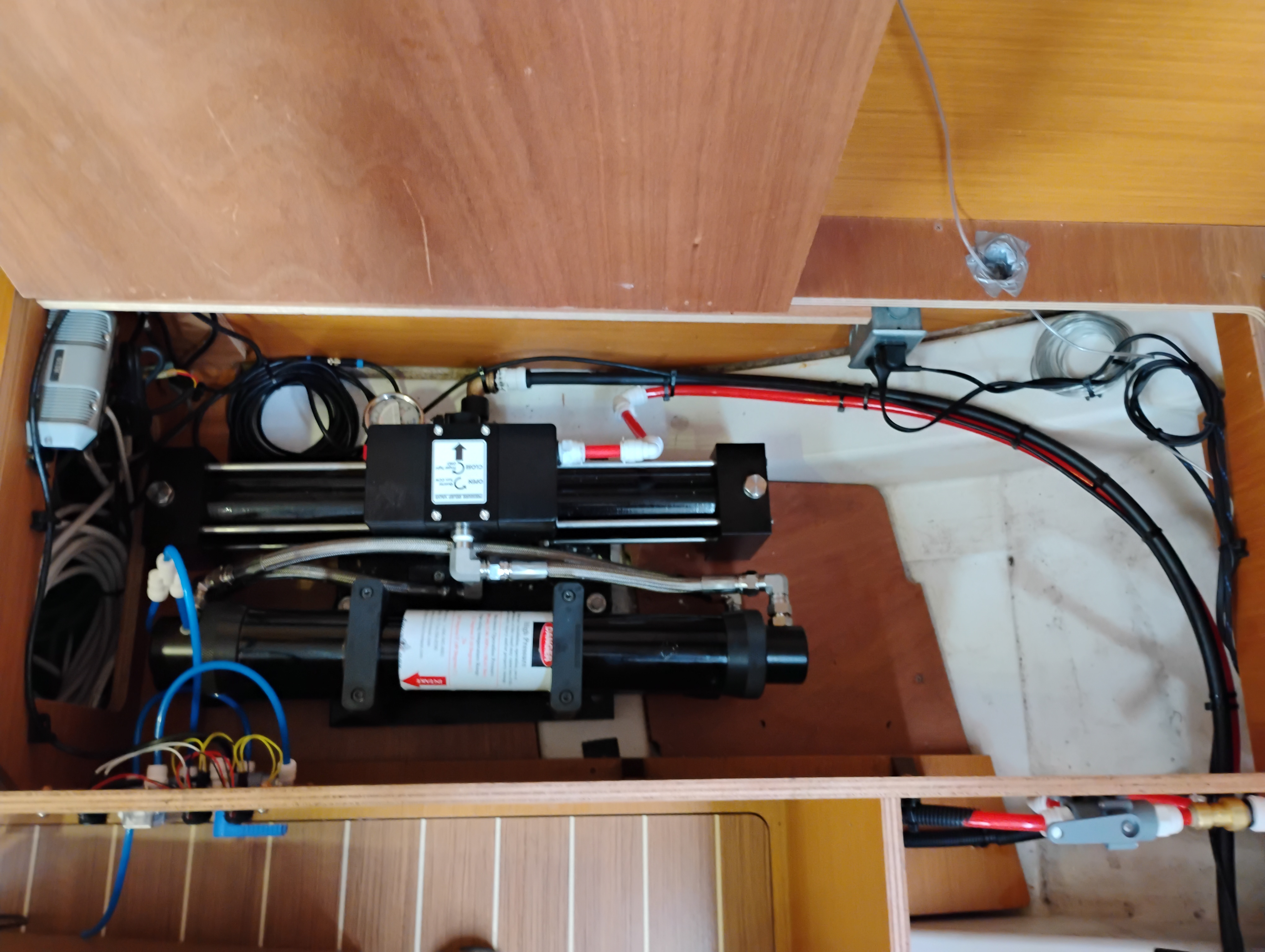 Watermaker high-pressure pump assembly mounted on a custom wood bulkhead with plumbing